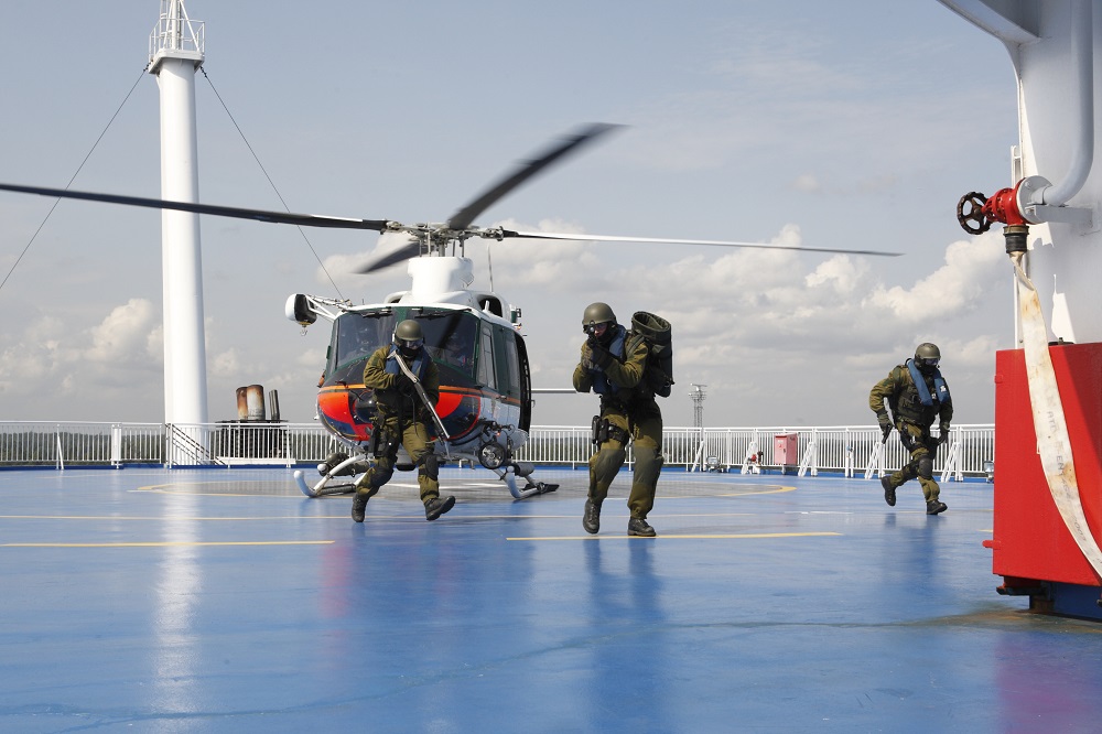 Three men are running on a ship’s helipad where a helicopter has landed.