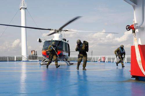 Three men are running on a ship’s helipad where a helicopter has landed.