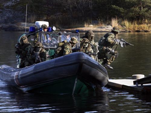 Five armed operators in camouflage uniforms jump from a speed boat to a pier.