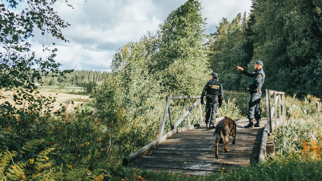 Kaksi rajavartijaa ja koira puisella sillalla.