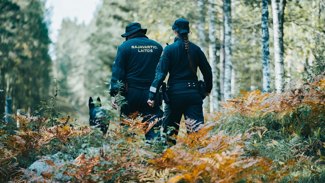 Kaksi rajavartijaa ja koira kävelevät maastorajalla.