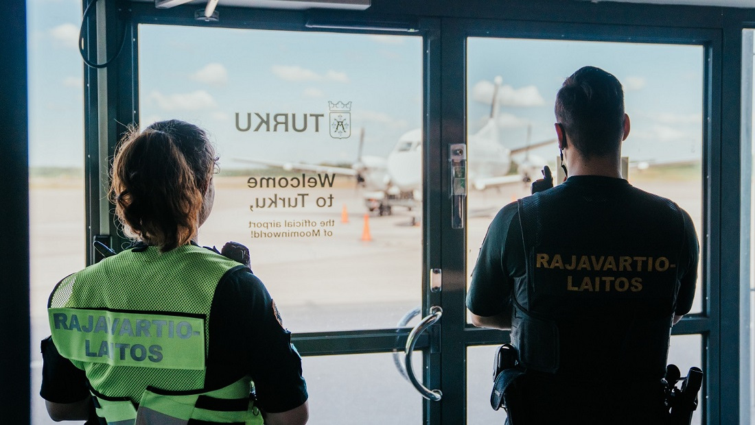Kaksi rajavartijaa katsoo lentoaseman ikkunasta selkä kameraan päin.