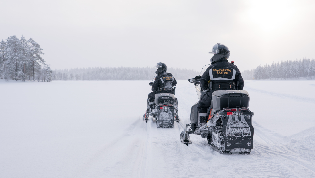 Kaksi rajavartijaa moottorikelkoilla lumisessa maisemassa.