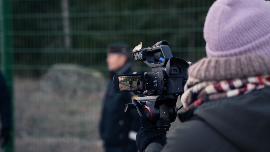 Journalisten filmar en gränsbevakare som står framför spärrstängslet.