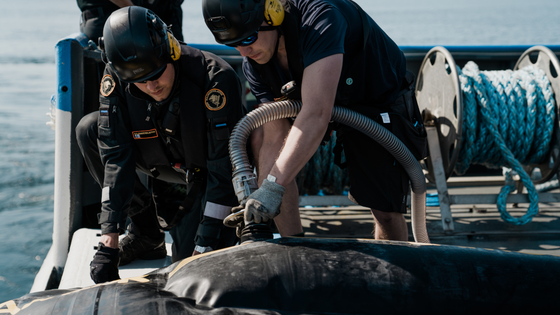 Två personer installerar en slang på fartygets däck för oljebekämpning.