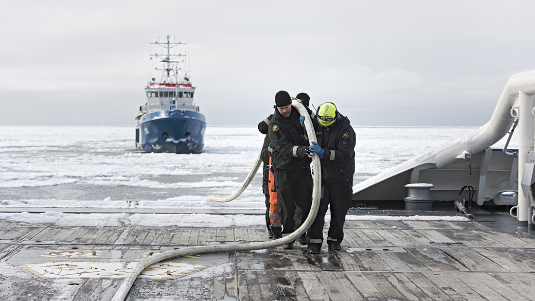 Henkilöt vetävät köyttä vartiolaivan takakannella. Takana jäinen meri ja ruotsalainen viranomaisalus.