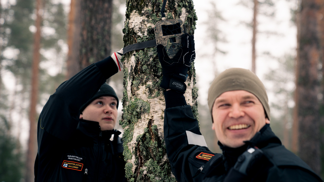 Rajavartijan peruskurssin opiskelijat metsässä kiinnittävät kameraa puuhun.