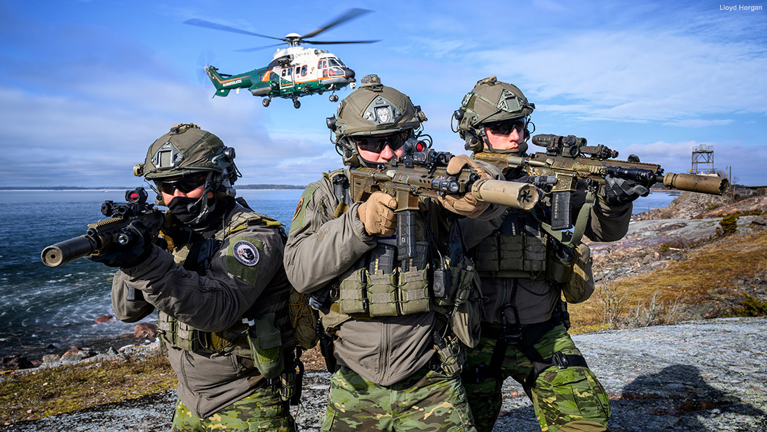 Rajavartiolaitoksen valmiusjoukkue harjoittelee kallioisella merenrannalla, taustalla helikopteri ilmassa.