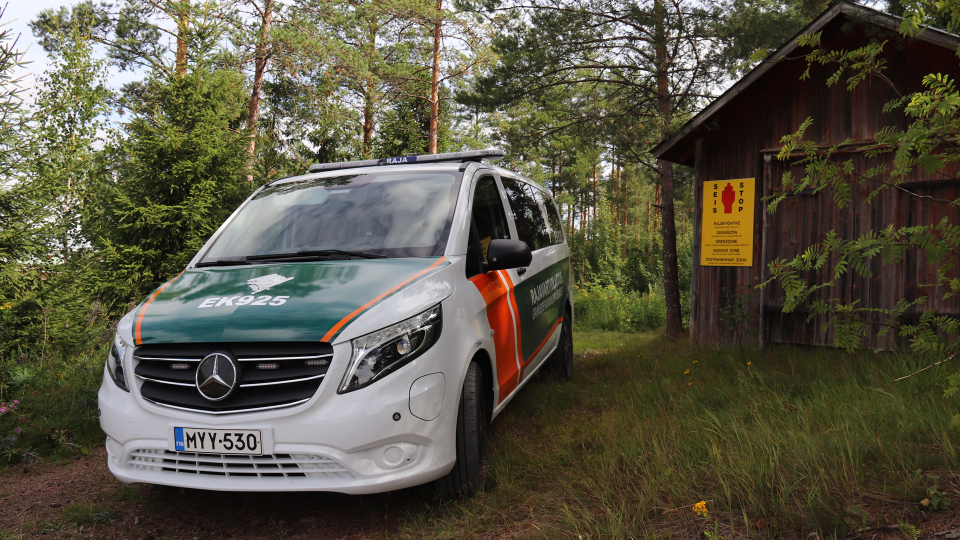 Gränsbevakningsväsendets elbil i skogen bredvid en byggnad av trä.