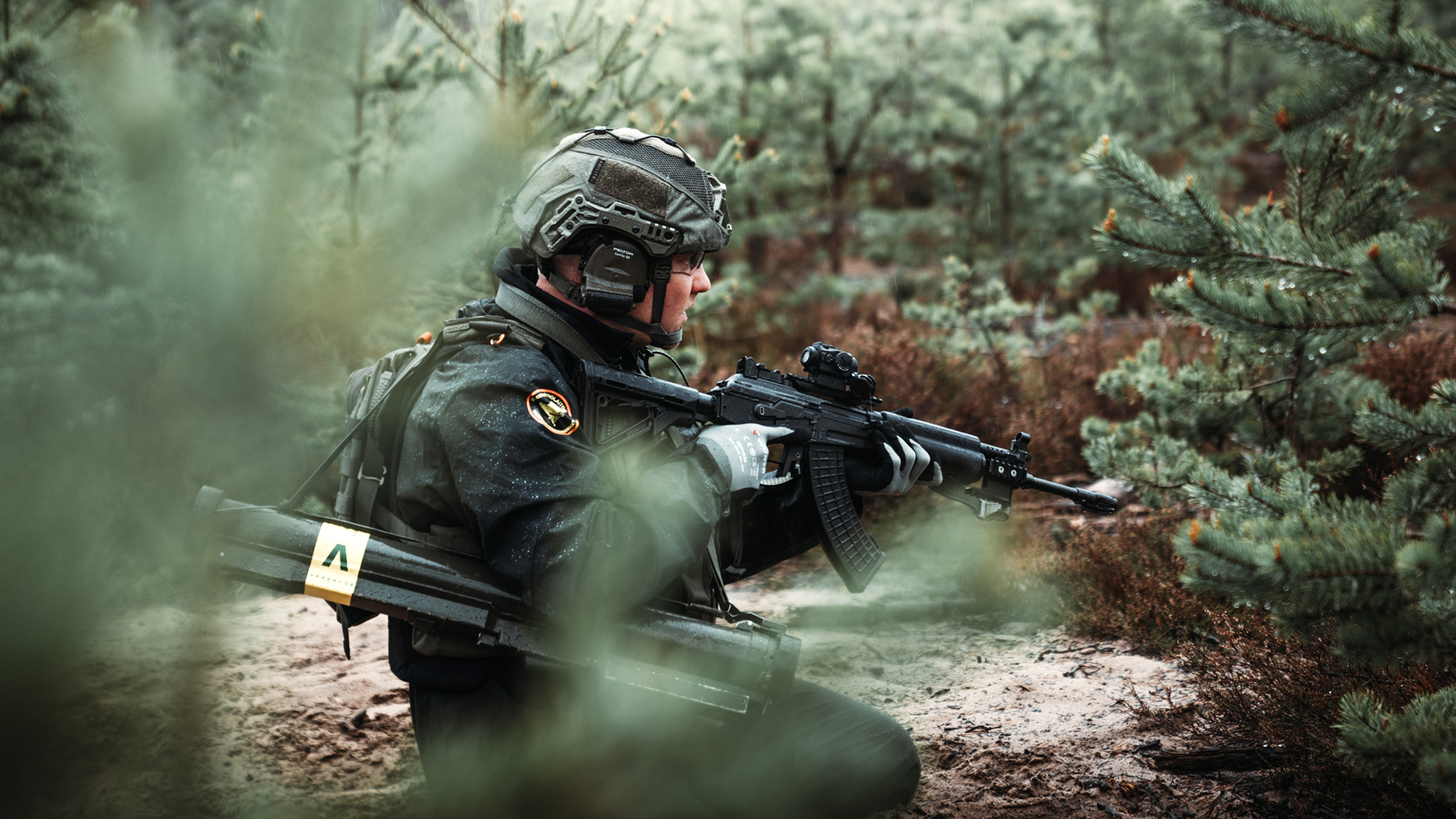 A border guard in a defence exercise in the woods. Surrounded by pines.