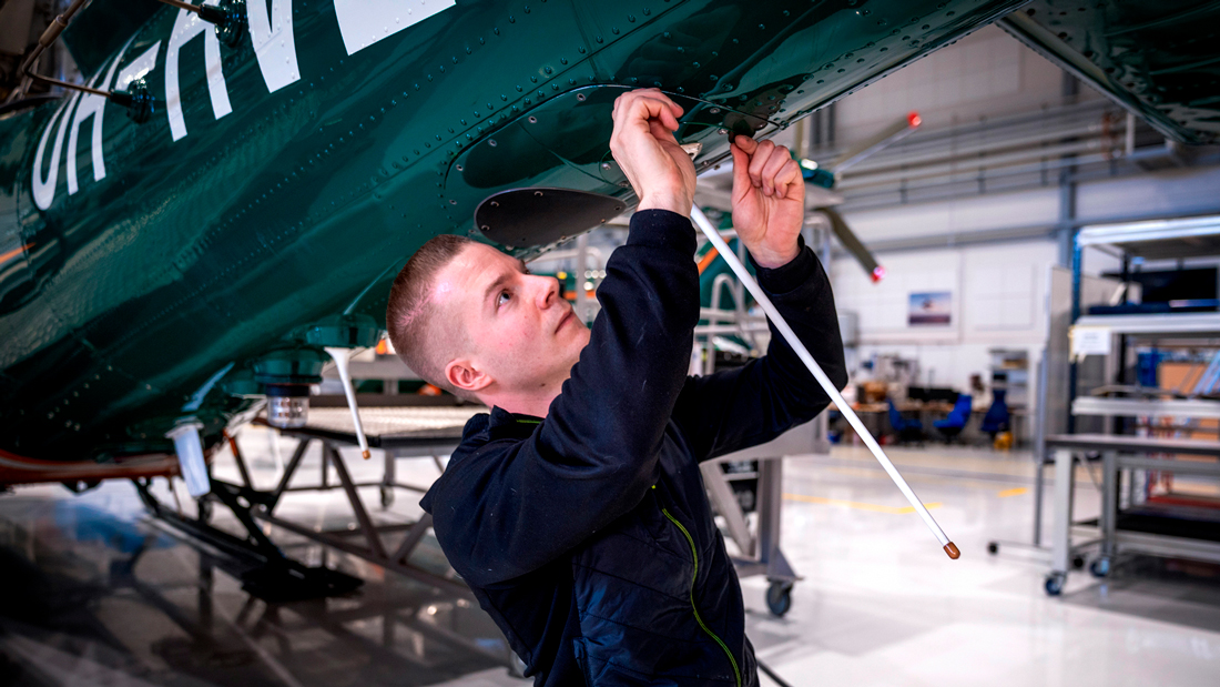 I halvfiguren tittar en ung man upp på helikopterns flygkropp och drar åt skruvar.