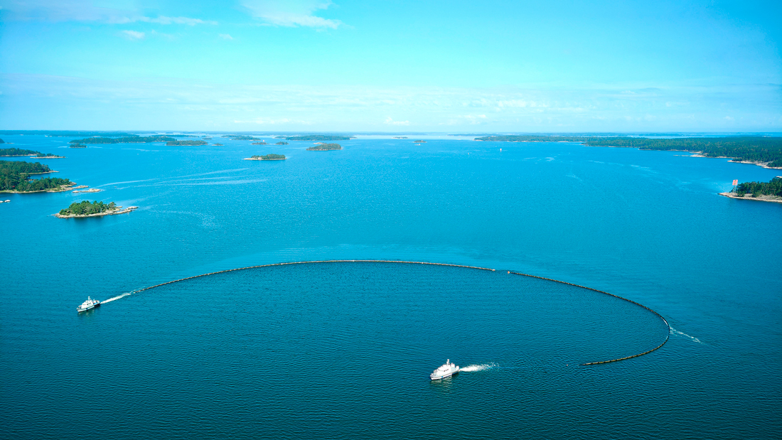 Två gränsbevakningsfartyg bogserar en oljeborrning i sommarskärgården. Foto taget ovanifrån.