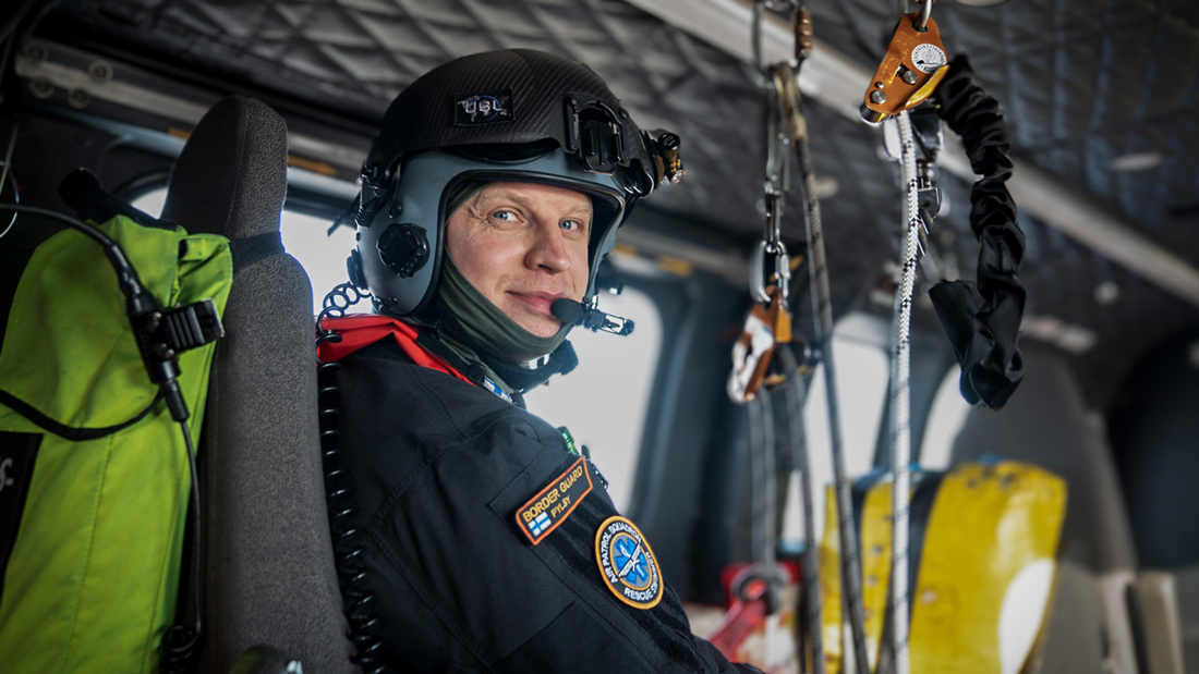 På halvfigursbilden sitter en yträddare ombord på en helikopter, iklädd utrustning, och tittar in i kameran med ett leende.