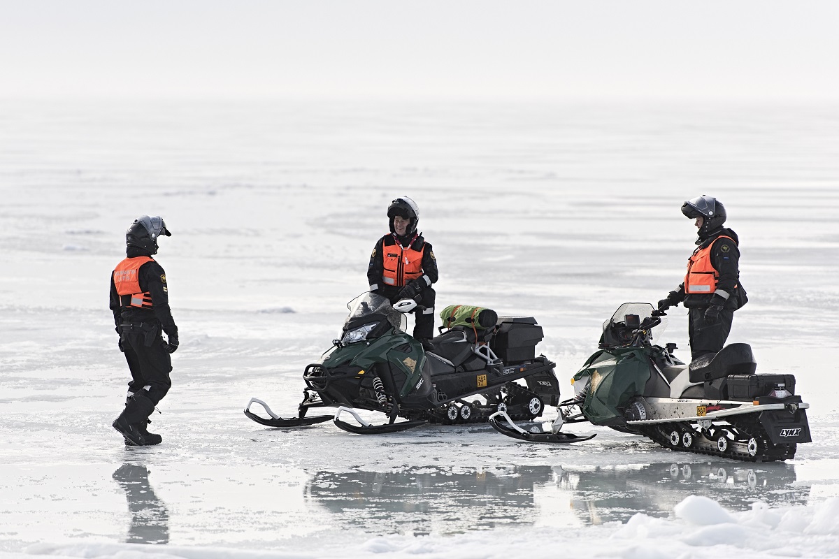 Kolme rajavartijaa huomioliivit päällä moottorikelkkojen vieressä jäällä.