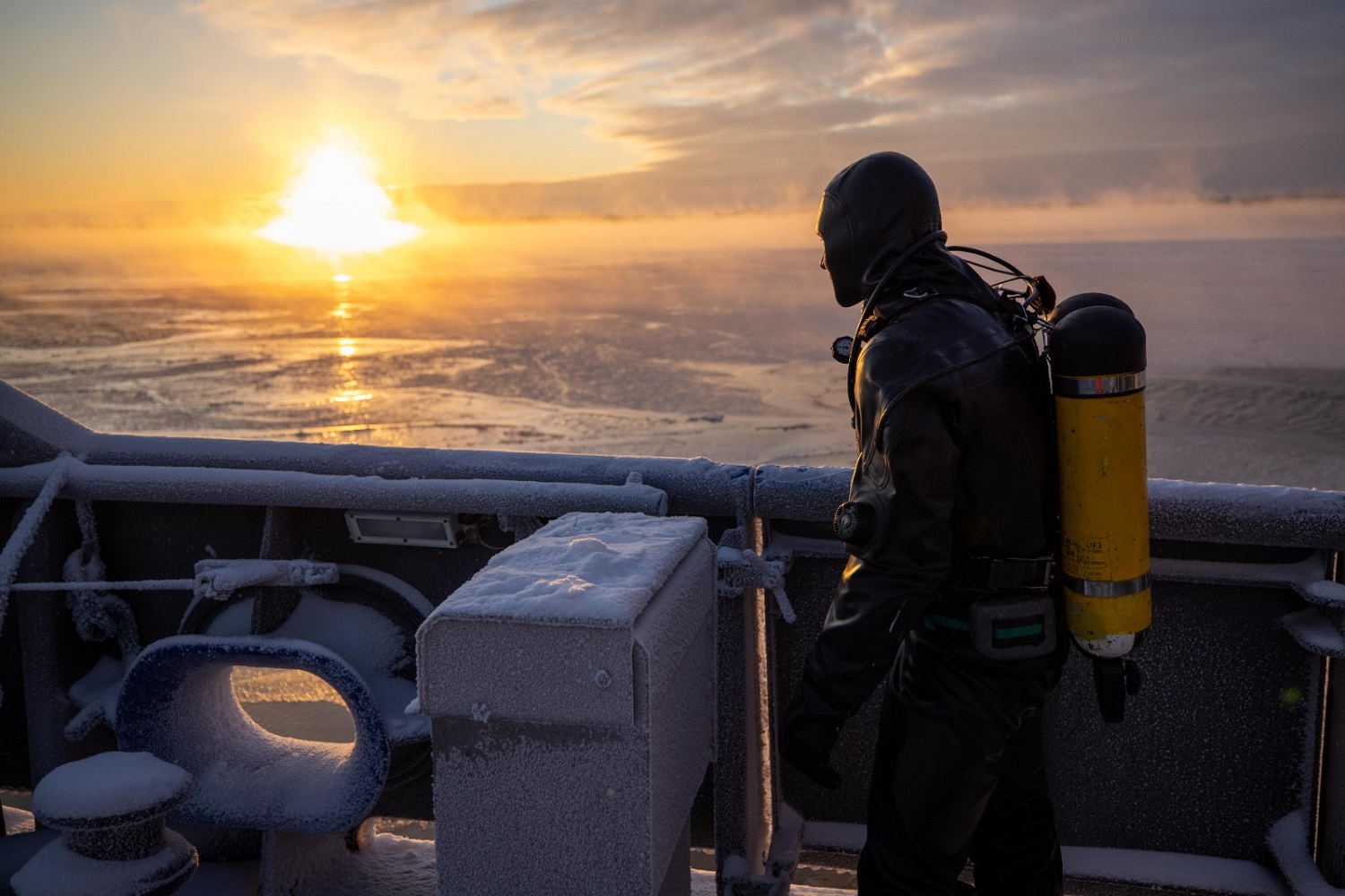 Sukeltaja katsoo auringon kajoa talvisella merellä laivassa.