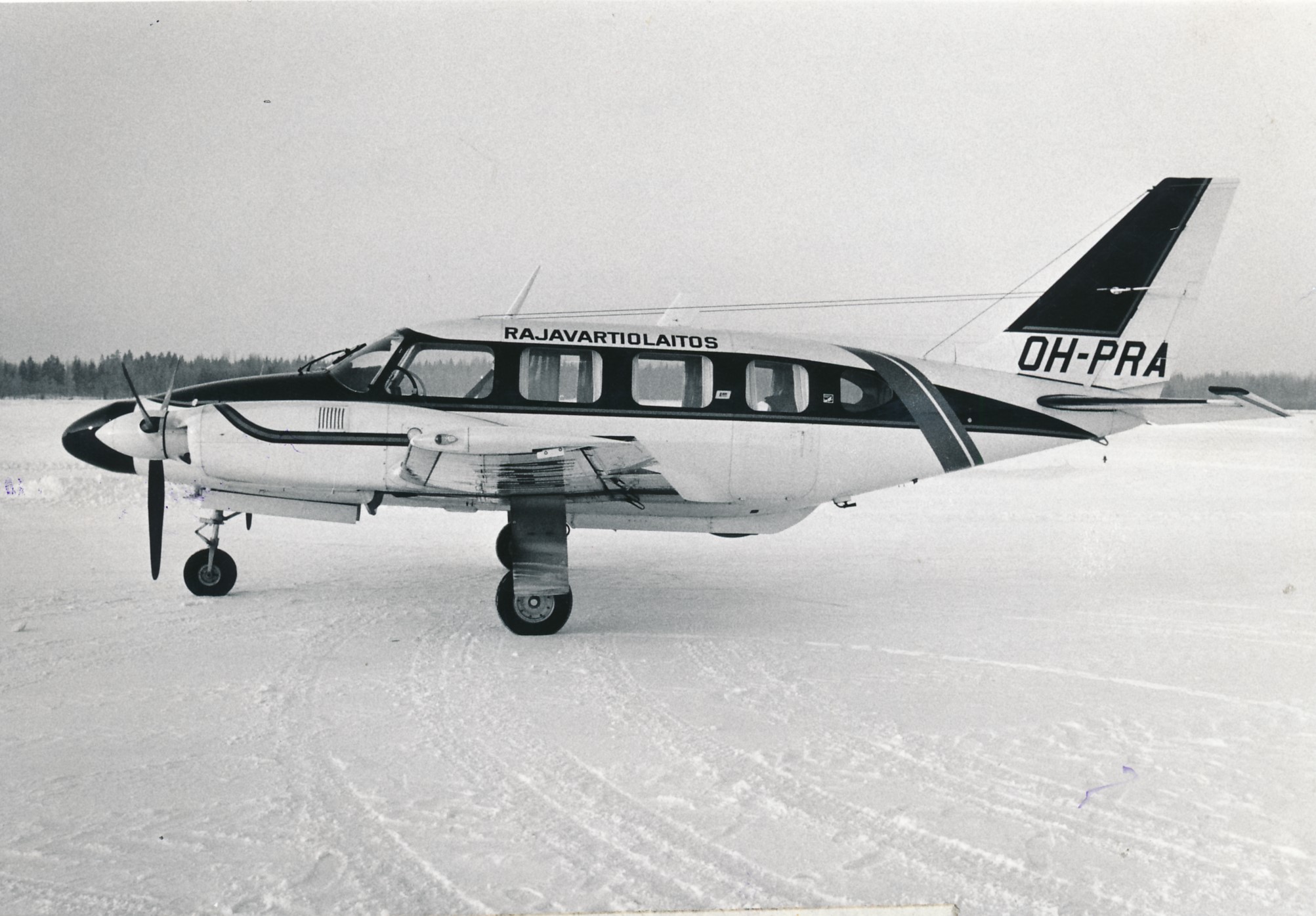 Sivustapäin kuvattu kaksimoottorinen lentokone talvimaisemassa. Koneen kyljessä teksti Rajavartiolaitos.