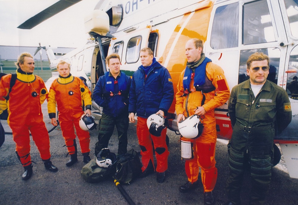 Gruppbild av sexmannabesättningen i helikoptern som deltog i räddningsarbetet med bilfärjan Estonia framför helikoptern.