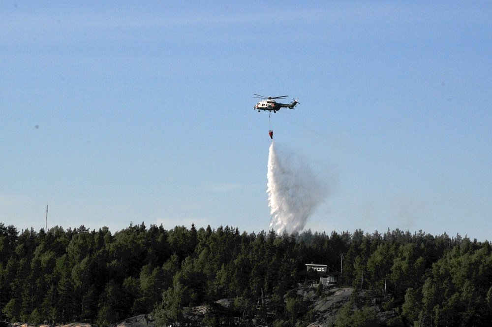 Helikopteri pudottaa sammutuspussista vettä palavan kesämökin päälle saaristossa.