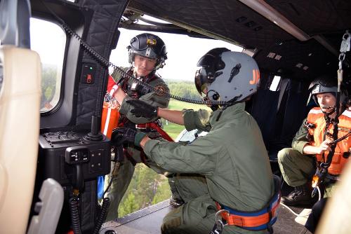 Fotografi taget inifrån en helikopter av besättningen i arbete. På bilden ser man tre medlemmar i besättningen, varav en håller på att vinschas ner.