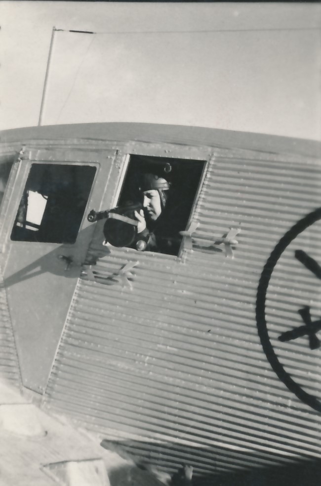 Close-up view from an aeroplane window. One of the aeroplane’s crew members is aiming their submachine gun out of the window.