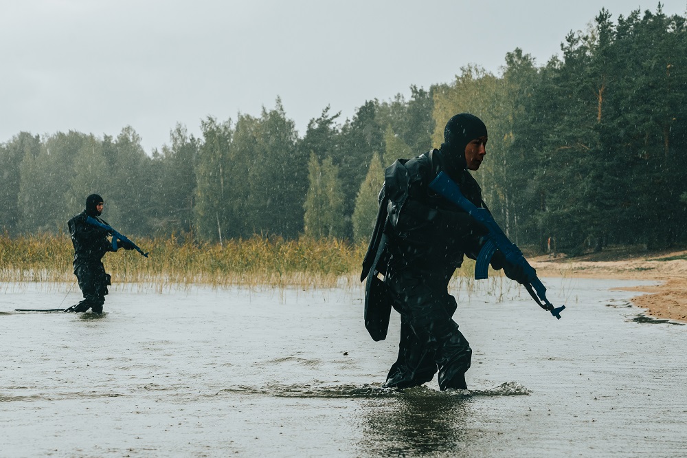 Kaksi erikoisrajajääkäriä kahlaa matalassa rantavedessä taisteluvarustuksessa.
