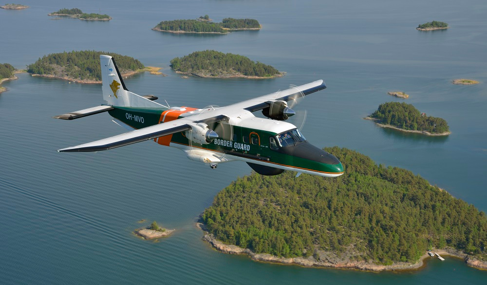 Ett Dornier-flygplan flyger över kusten i soligt väder.