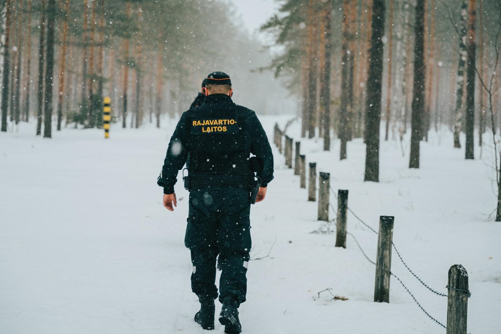 Kaksi rajavartijaa kävelee raja-aidan vieressä. Sataa lunta.