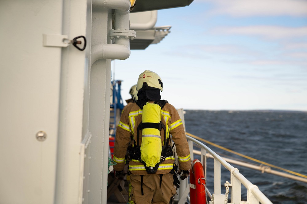 Suojapukuinen henkilö kävelee kannella happisäiliö selässä.