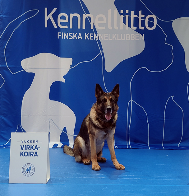 Clapton poseeraa vuoden virkakoira kyltti vierellään.