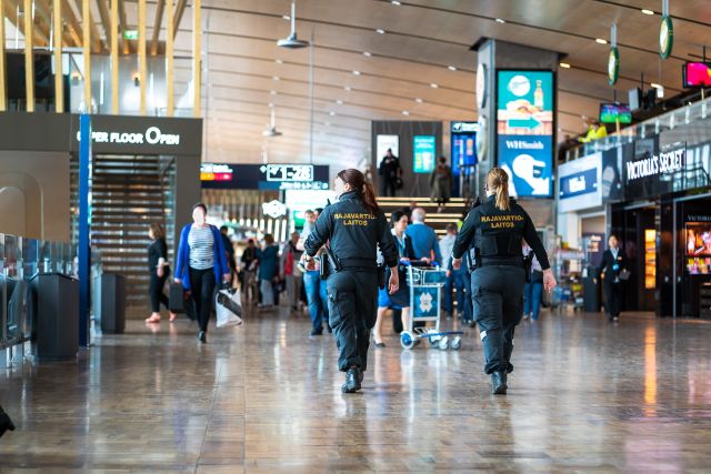 Kaksi merivartijaa kävelee lentoaseman terminaalissa. Taustalla lentoa odottavia matkustajia.