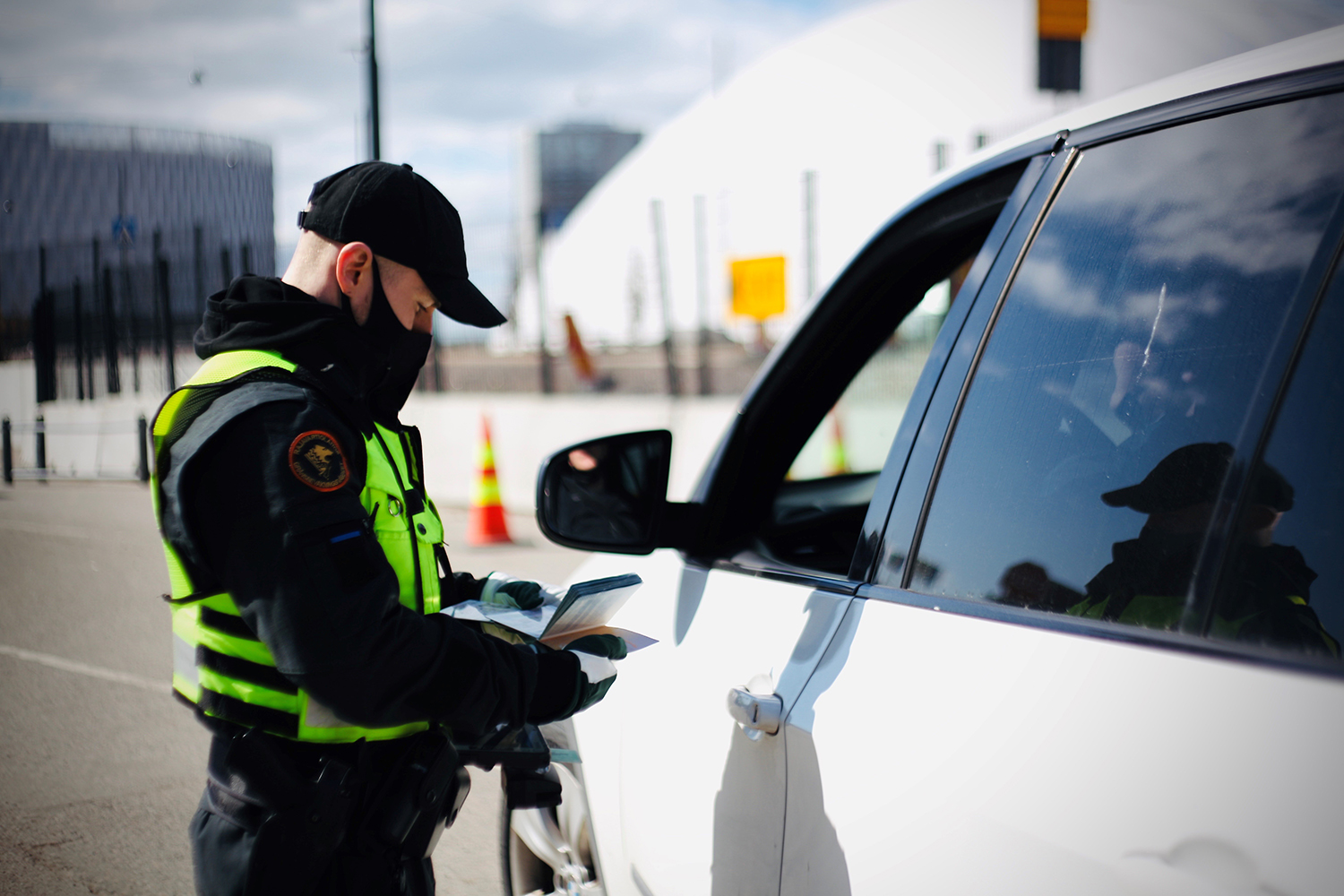 En gränskontrollant undersöker en bilresenärs resedokument bredvid bilen. 