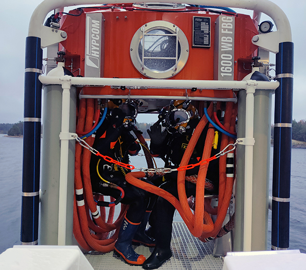 Två dykare dyker i en våtklocka i havets djup.