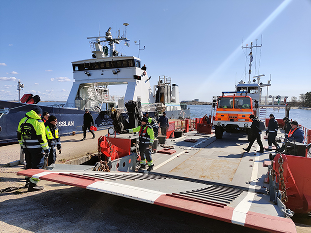 Människor och en lastbil lämnar räddningsverkets fartyg. I bakgrunden avtalsfartyget Grisslan.