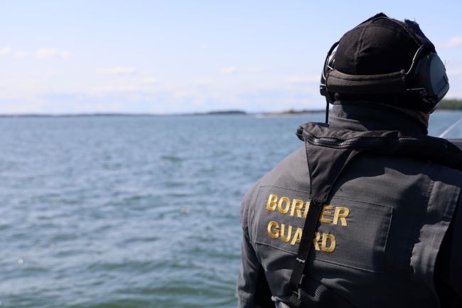 Rajavartija kuvan oikeassa reunassa selin kameraan. Taustalla aava meri.