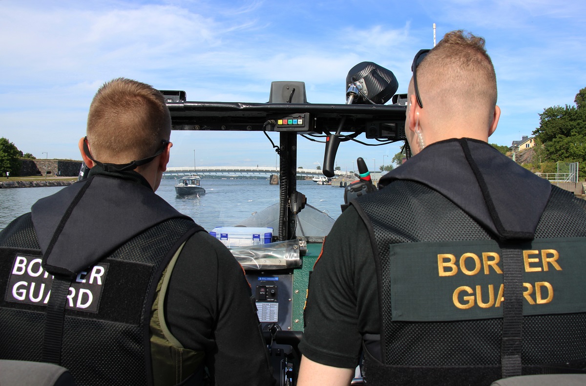 Kaksi rajavartijaa ajaa veneellä tarkkaillen merellä liikkuvia veneilijöitä.