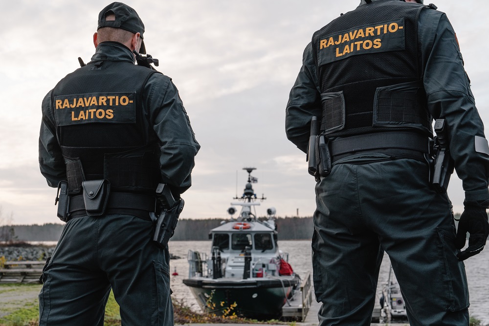 Kaksi merivartijaa seisomassa meren äärellä. Partiovene kiinnitettynä laituriin.