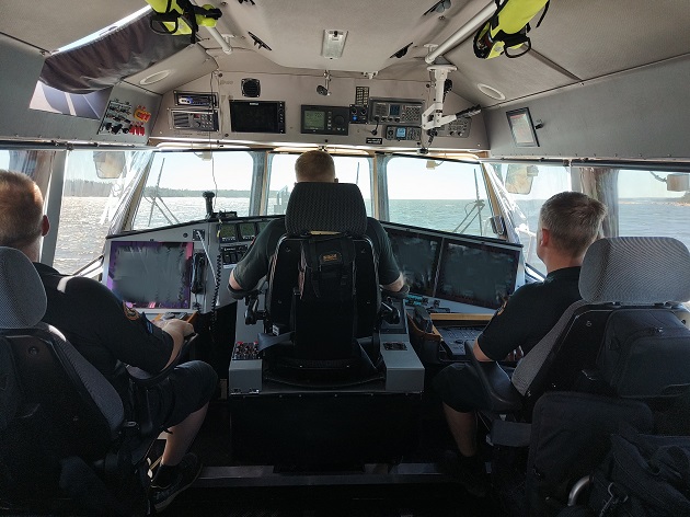 Tre sjöbevakare i förarhytten på en patrullbåt.