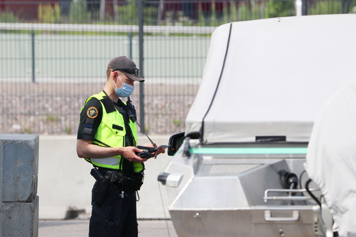 En gränsbevakare med ansiktsskydd står bredvid en bil i hamnen och granskar resedokumentet.