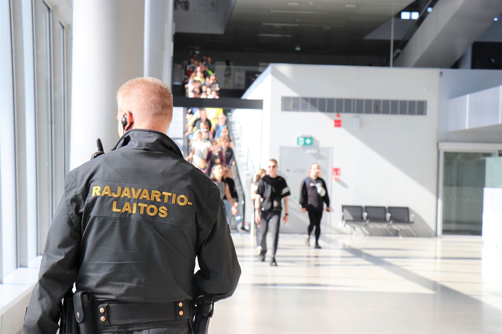 Rajavartija satamaterminaalissa. Taustalla joukko ihmisiä.
