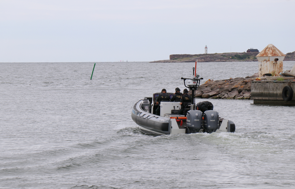 Tre sjöbevakare med ryggen mot kameran i en snabb båt på havet.