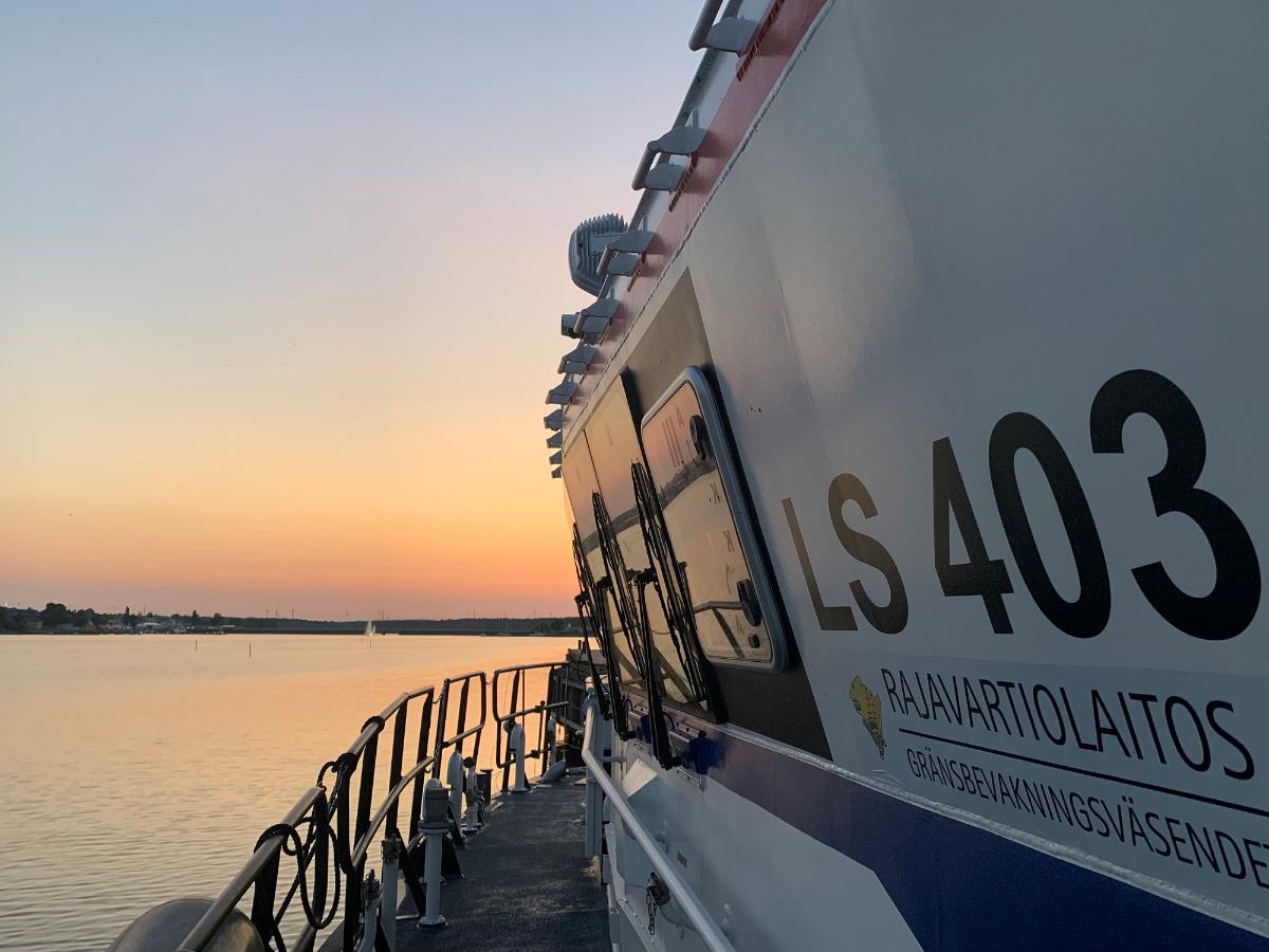 Sjöbevakningssektionens båt fotad från sidan. Bakom syns en orange solnedgång.