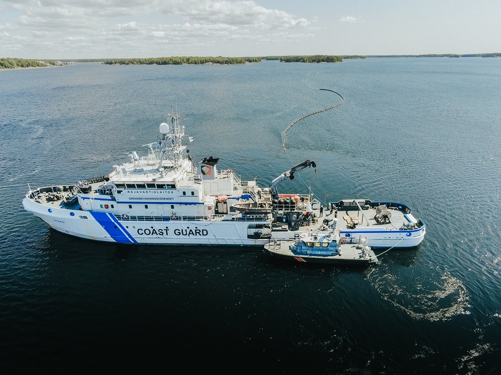 Ilmakuva vartiolaivasta, jonka kyljessä kiinni partiovene. Laivan toisella laidalla öljypuomi levitettynä.