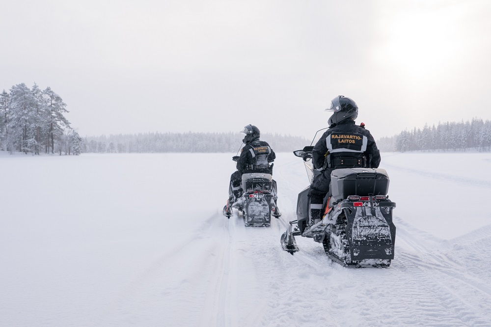 Two border guards riding snowmobiles in the border strip and moving toward the photographer.