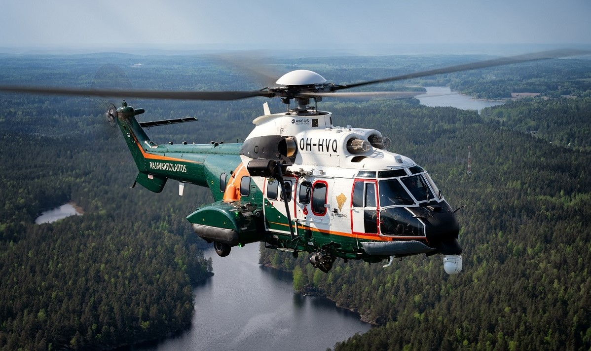 A Super Puma helicopter from the Finnish Border Guard flying over a forest landscape.