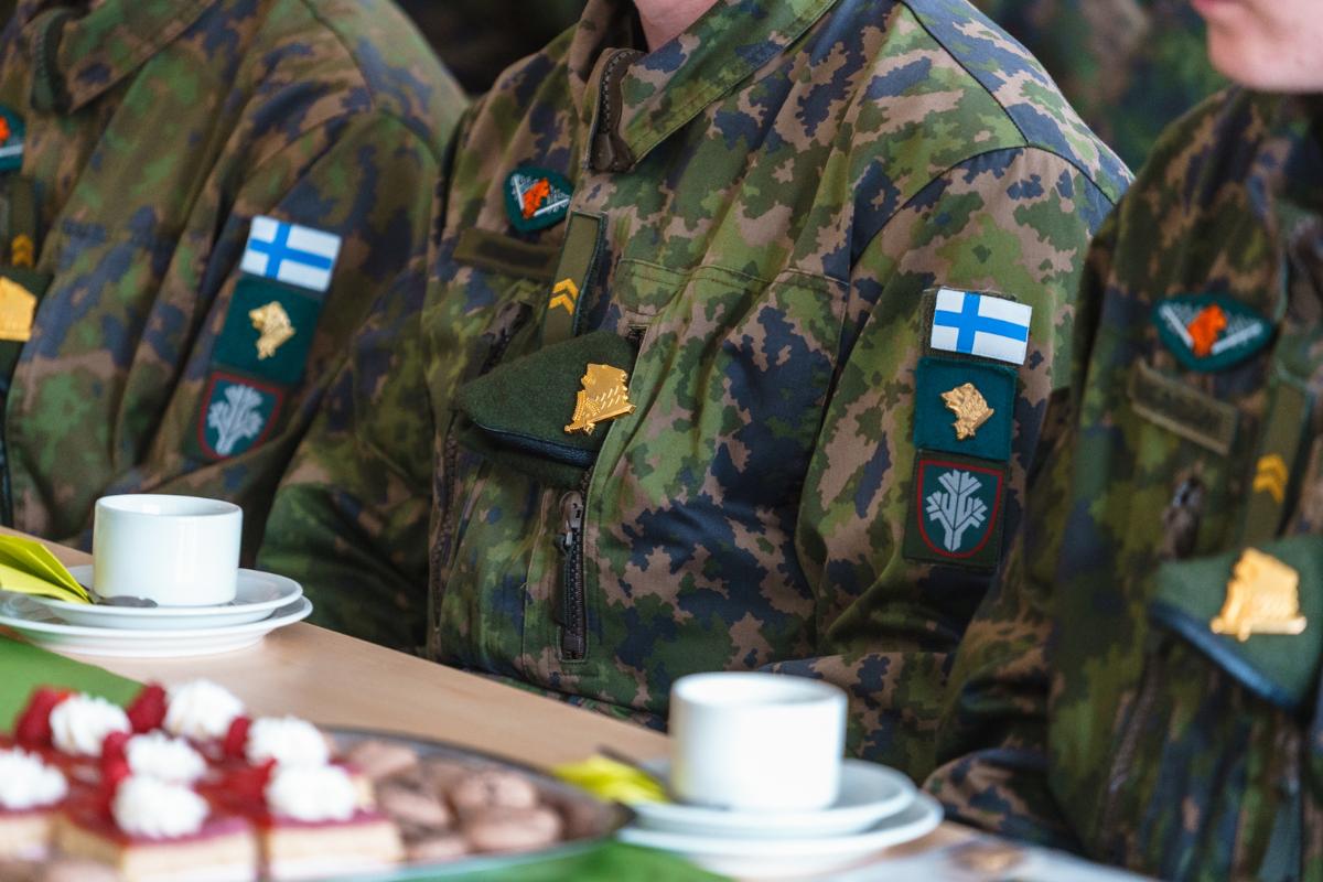 Lähikuva kolmen kahvipöydässä istuvan varusmiehen palveluspuvuista, joissa on karhunpäätunnus ja sissihavumerkki.