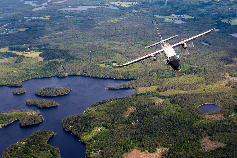 Flygplan över ett skogbevuxet sjölandskap.