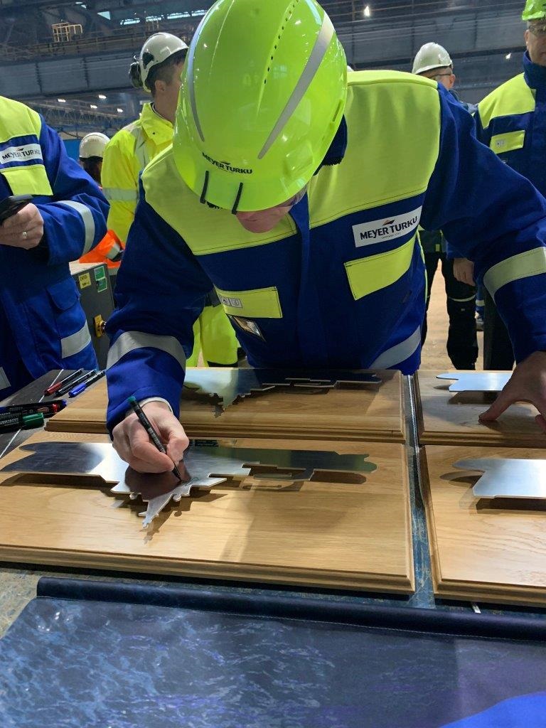 Kypäräpäinen mies kirjoittaa nimensä metalliseen laattaan.