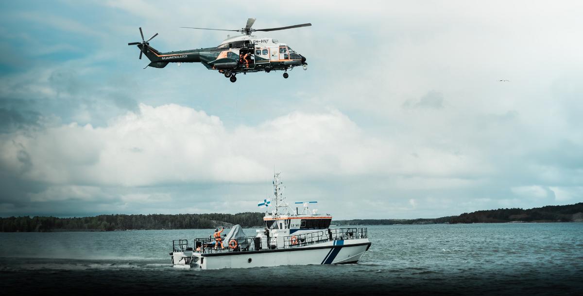 A patrol boat and a helicopter flying above it.