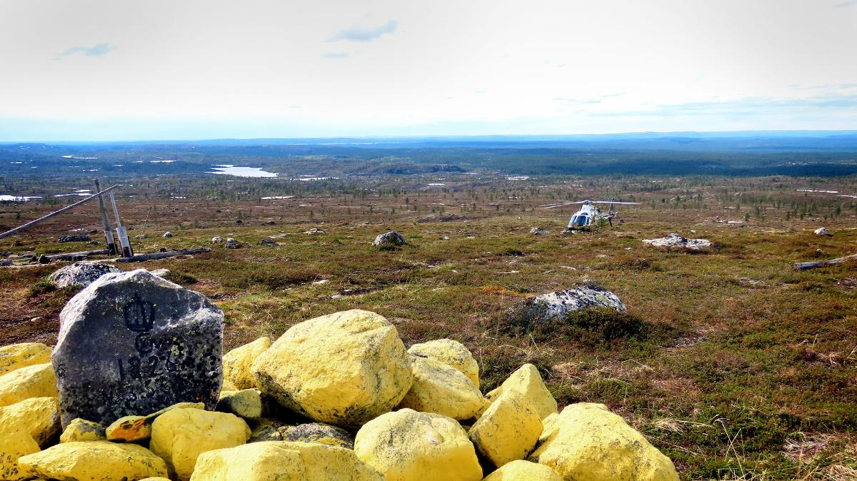 Pohjoinen tundramaisema, etualalla rajakiviä ja taaempana Rajan helikopteri