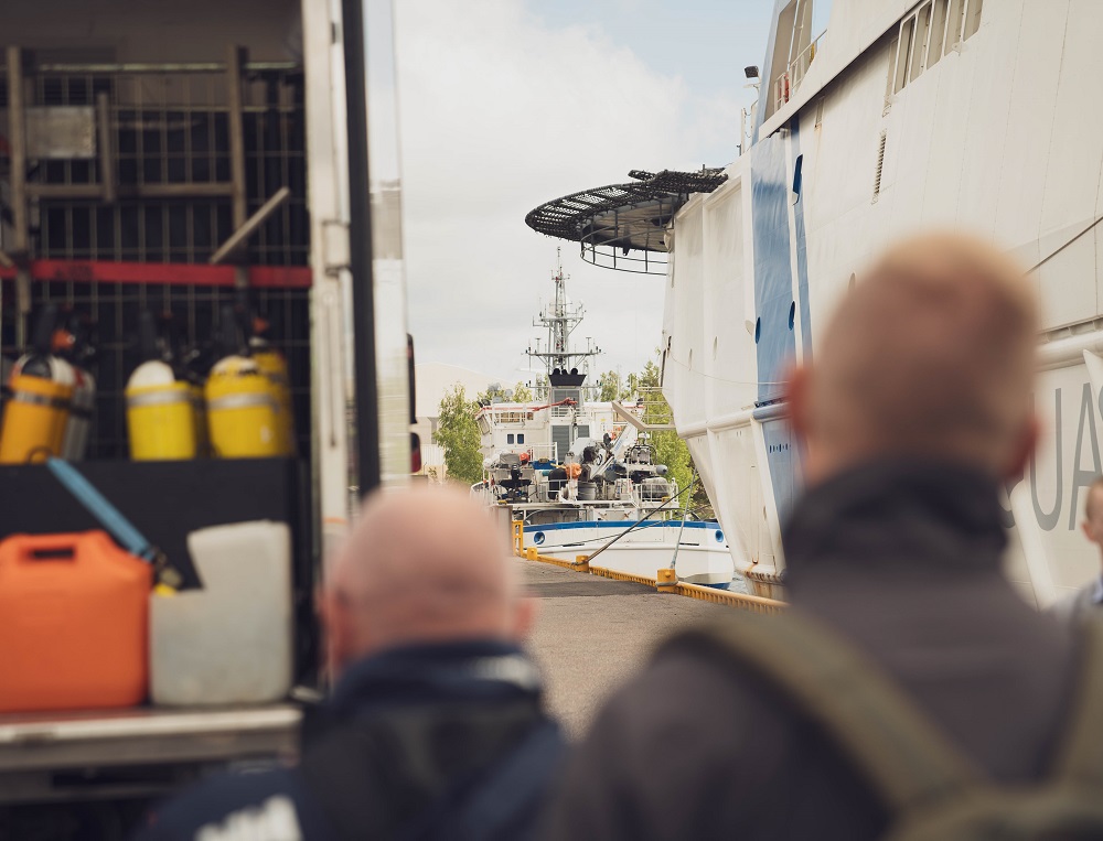 Two people are watching a patrol ship and a patrol boat at the harbour.